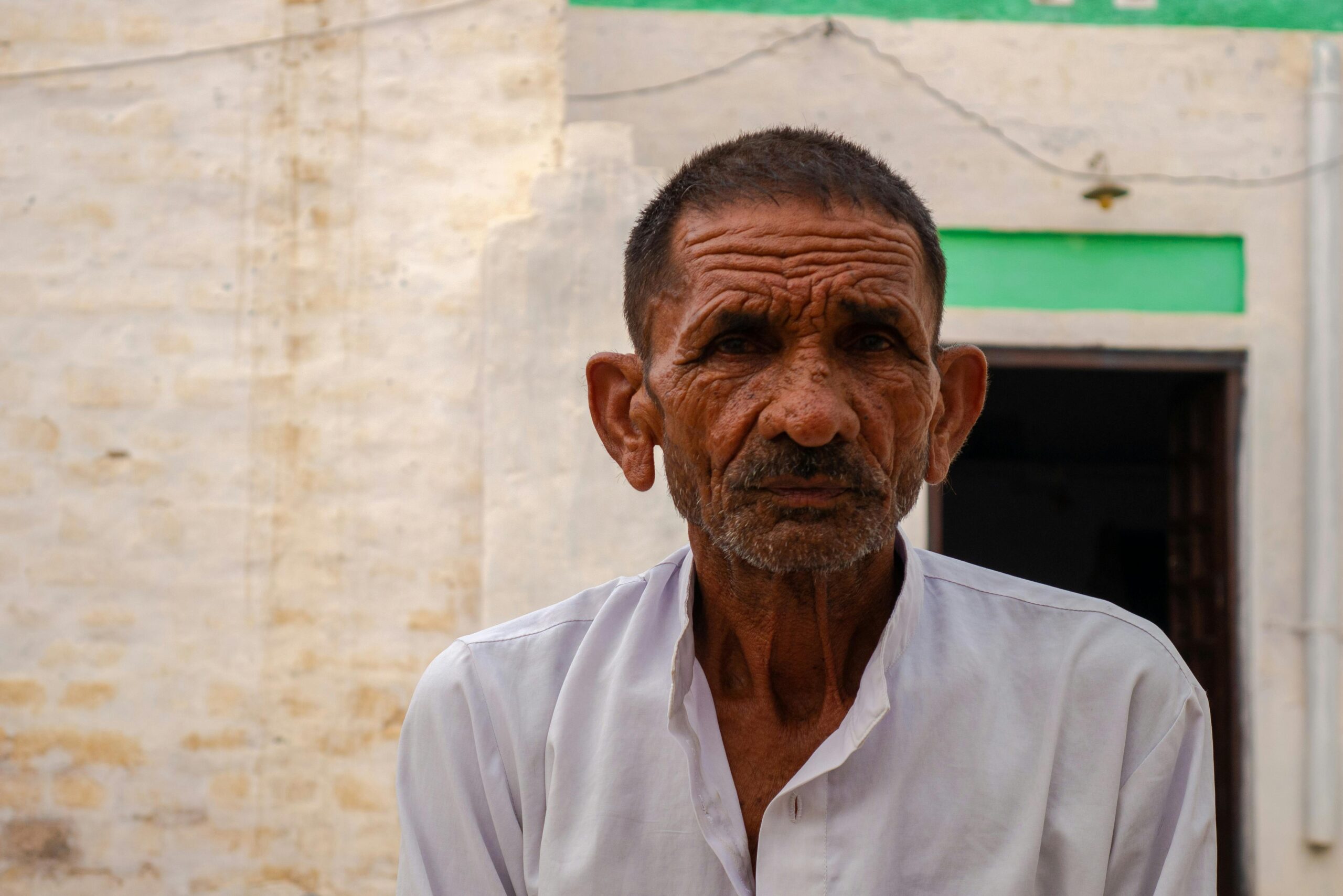 Close-up portrait of an elderly Indian man with wrinkles in a white shirt, outdoors.